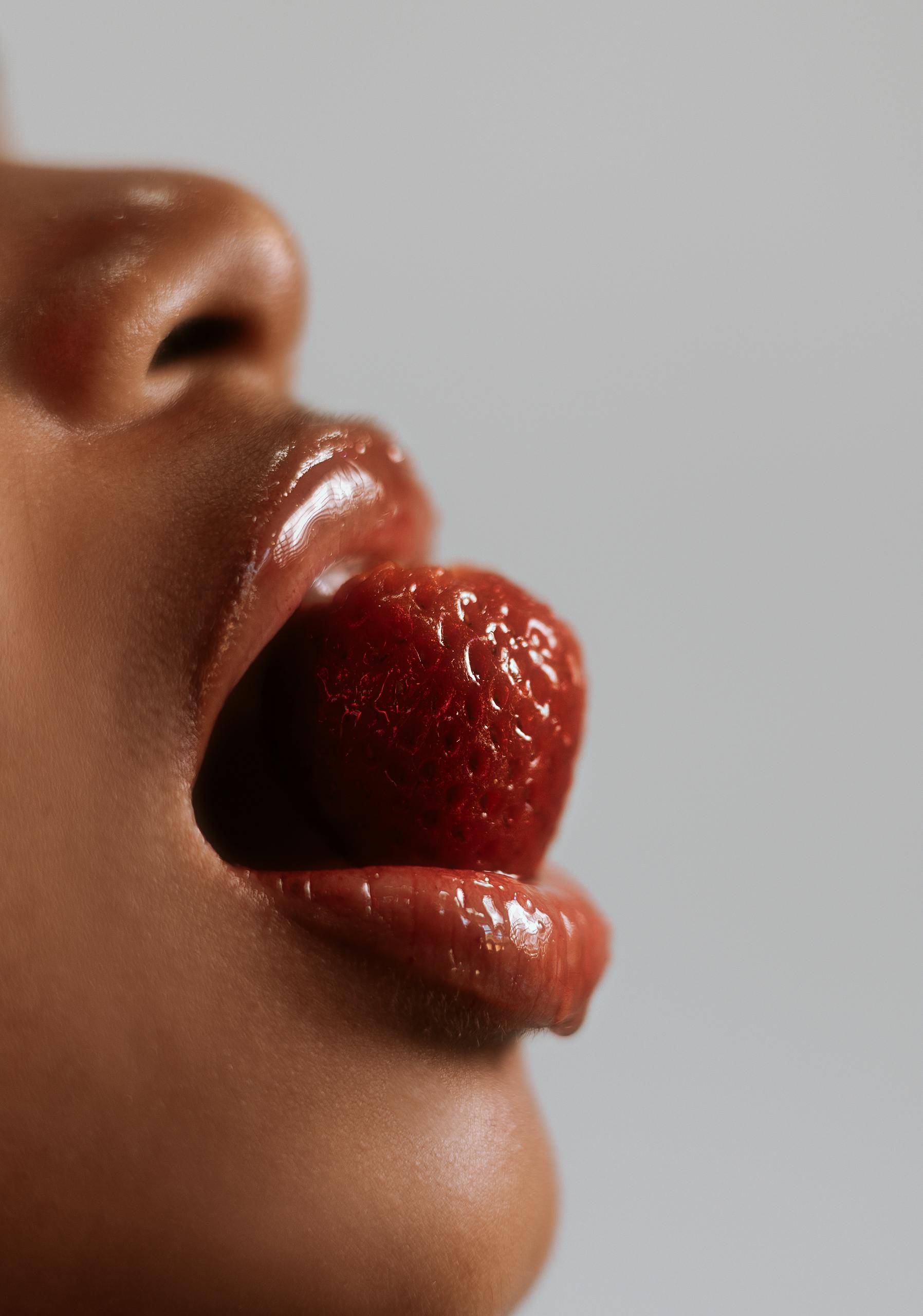 Artistic close-up of lips holding a strawberry, emphasizing sensuality and texture.