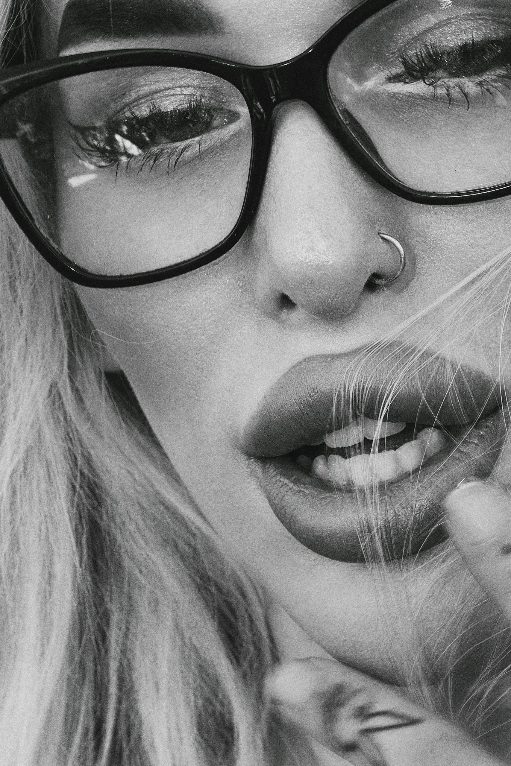 Black and white close-up of a young woman wearing eyeglasses and a nose ring.